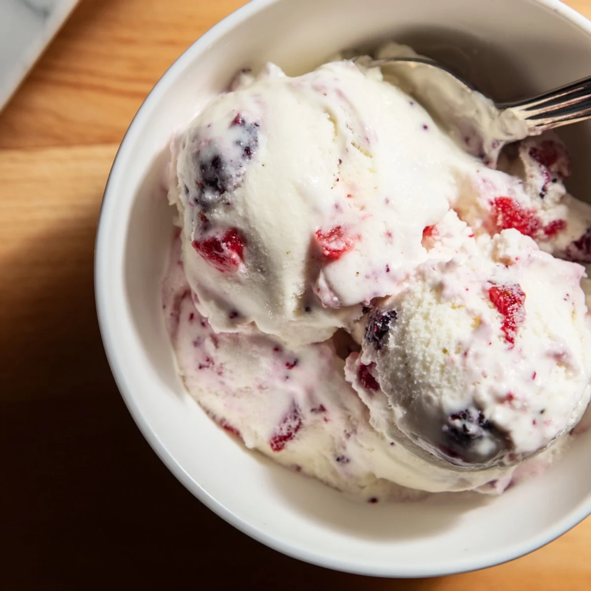 Scoops of creamy cottage cheese ice cream, with mixed berries shown on a white serving dish.