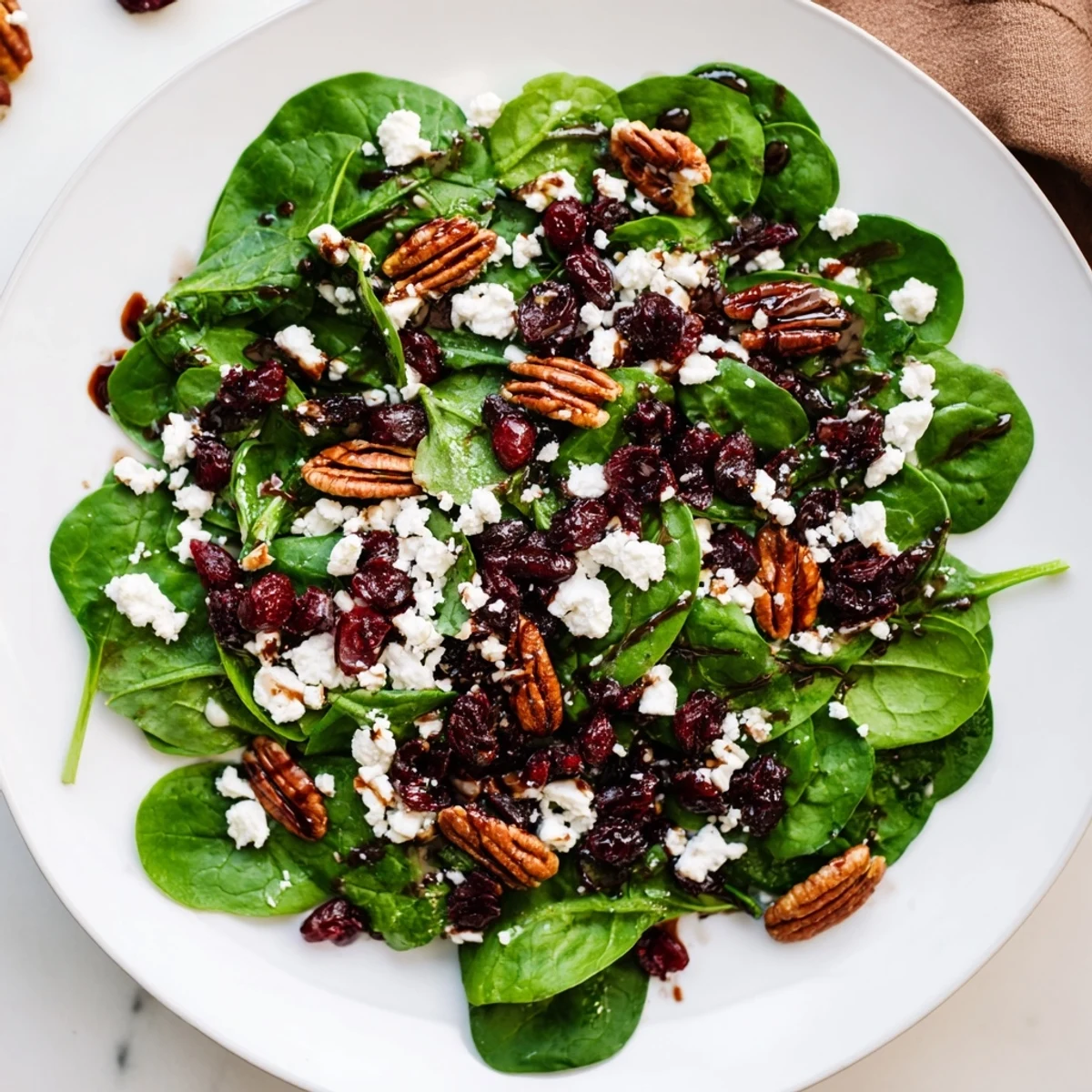 Fresh Spinach Goat Cheese Salad glistening with balsamic vinaigrette, featuring crumbled goat cheese, sweet dried cranberries, and chopped candied pecans for a vibrant bite.