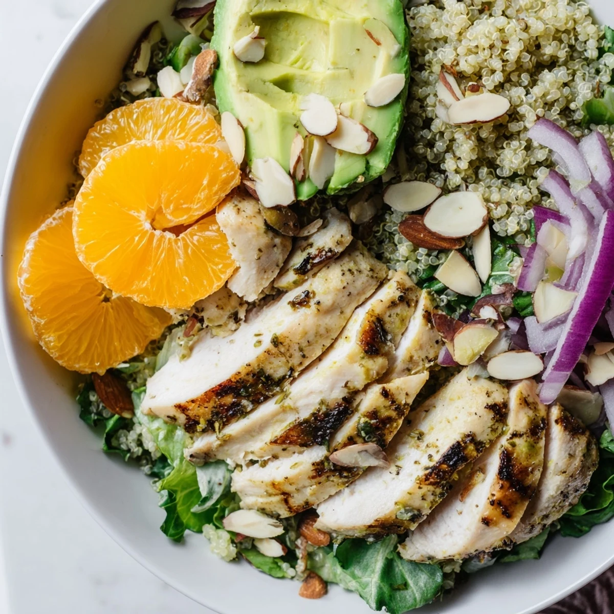A healthy, gluten-free meal featuring sliced grilled chicken over fluffy quinoa, crisp greens, avocado, and a zesty citrus vinaigrette.