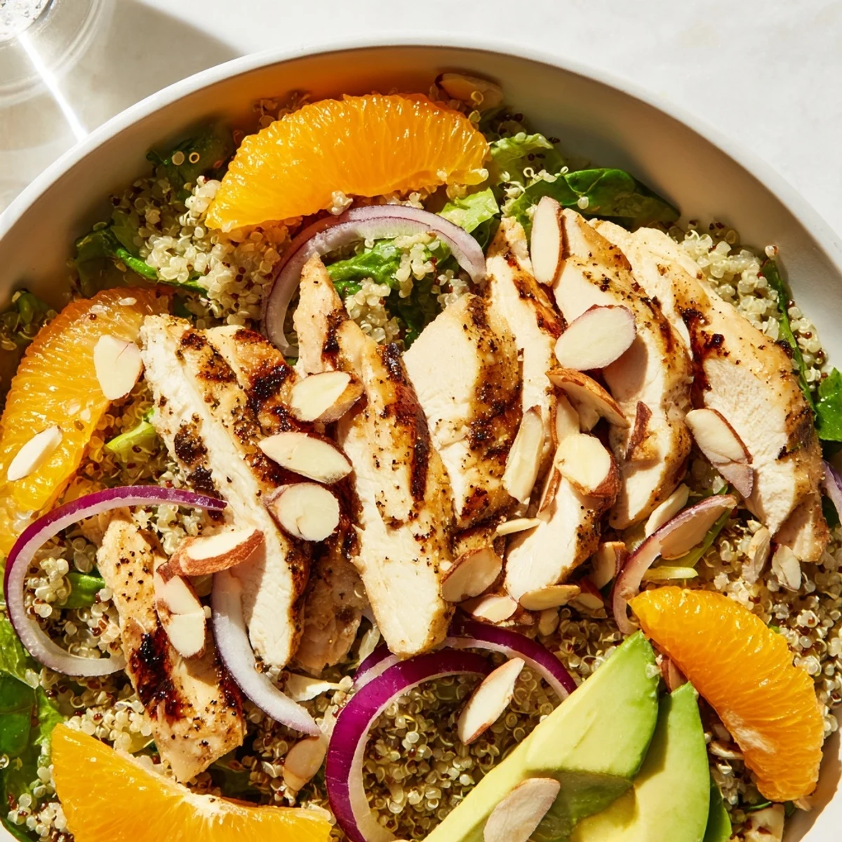 Colorful bowl of grilled Citrus Herb Chicken Salad with red onion, toasted almonds, and vibrant orange slices on a bed of greens.