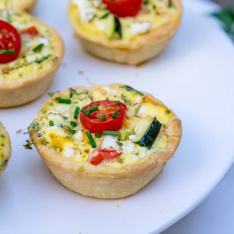 A colorful photo displays homemade Couronne Florale Mini Quiches, filled with spring vegetables and creamy cheese.