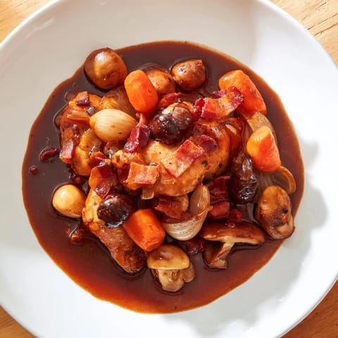 Golden-brown chicken pieces and mushrooms simmering in a fragrant Coq au Vin stew.