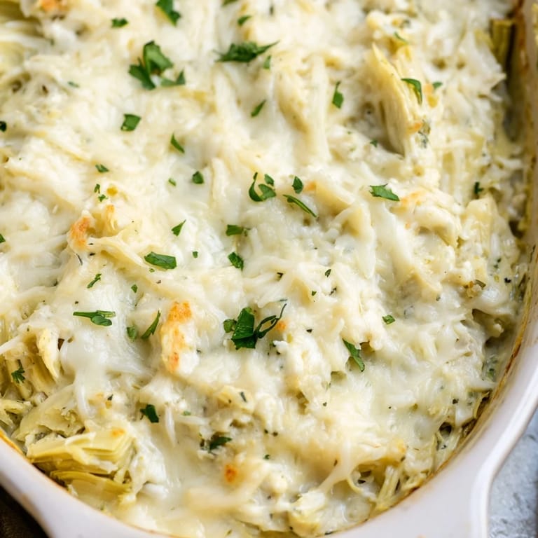 Warm, irresistible Baked Artichoke Dip, garnished with parsley, being served with toasted baguette slices.