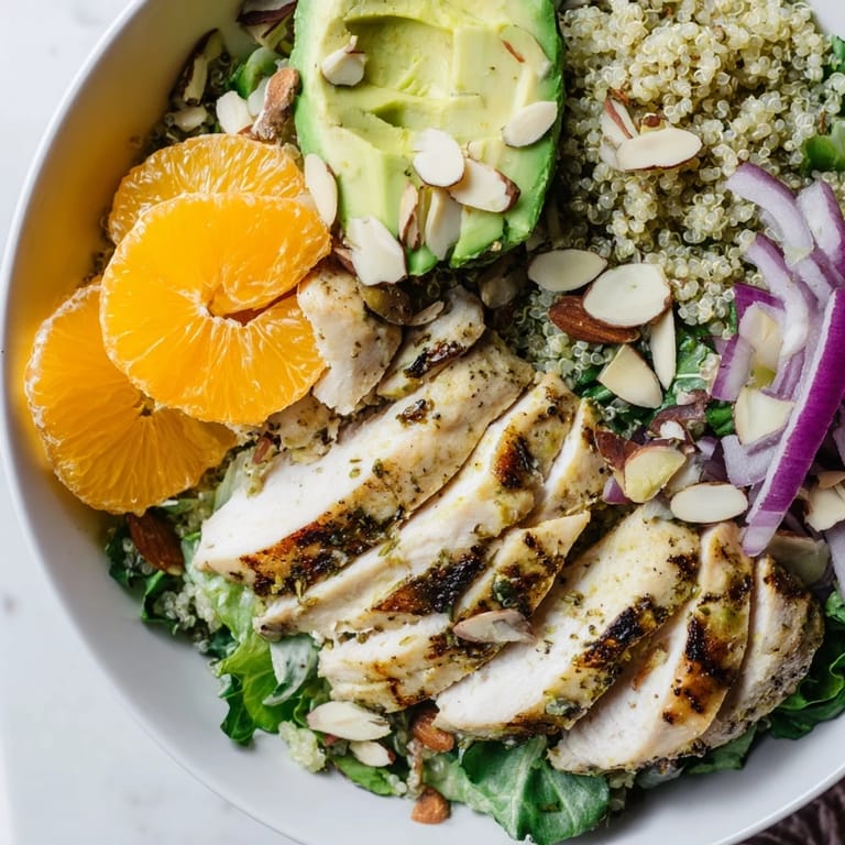 A healthy, gluten-free meal featuring sliced grilled chicken over fluffy quinoa, crisp greens, avocado, and a zesty citrus vinaigrette.