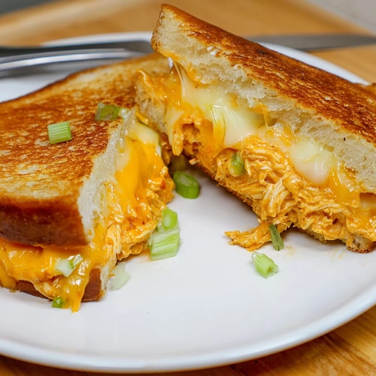 A close-up of Buffalo Chicken Ranch Grilled Cheese, showcasing crispy sourdough and gooey cheddar with a side of celery sticks.